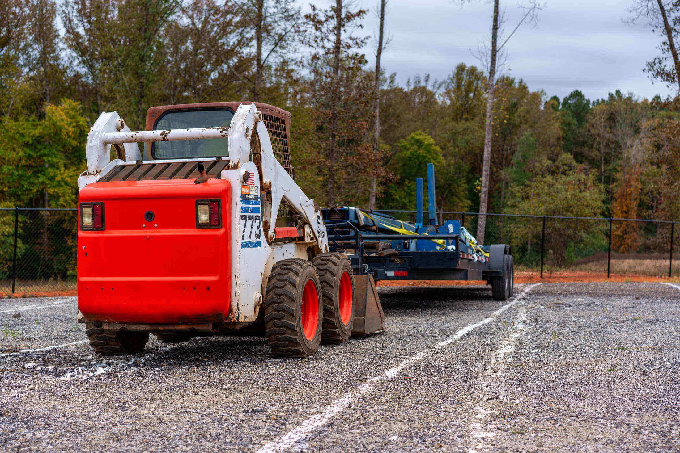 Skid steer loader towing equipment on gravel.