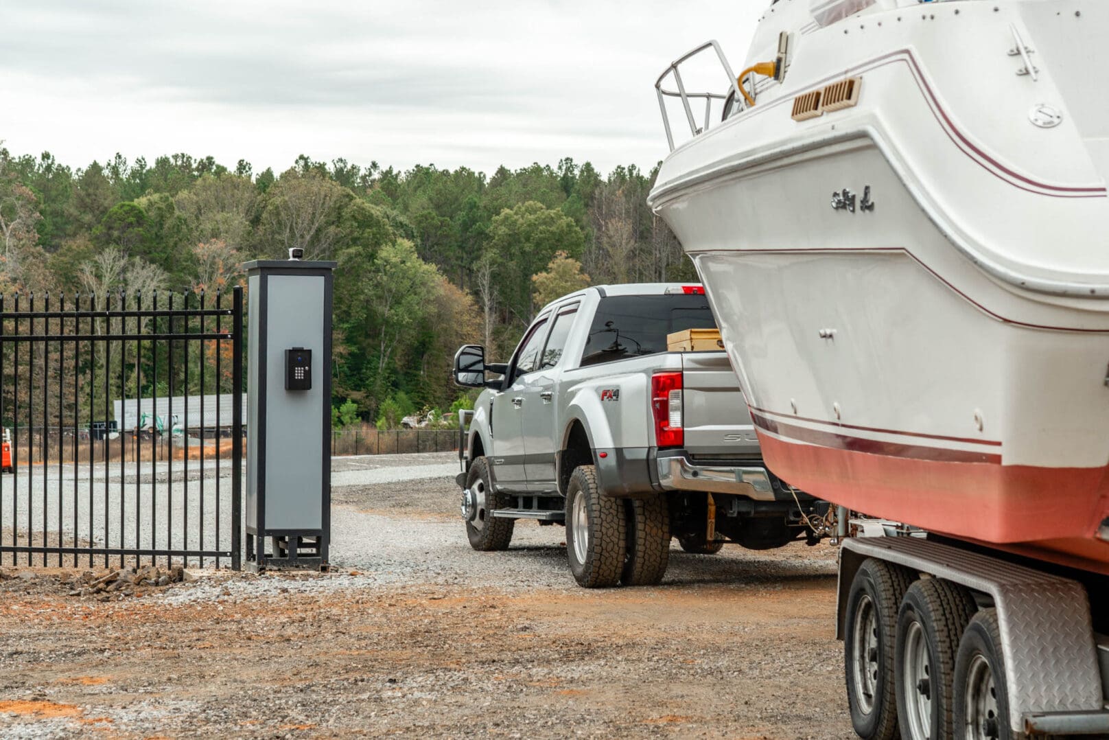 Truck towing boat near gated entrance.